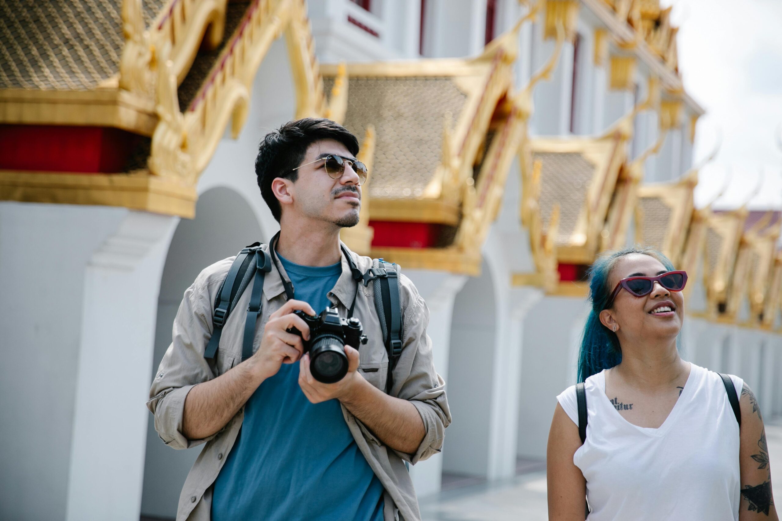 Two tourists with cameras enjoy a sunny day at an ornate Asian temple.